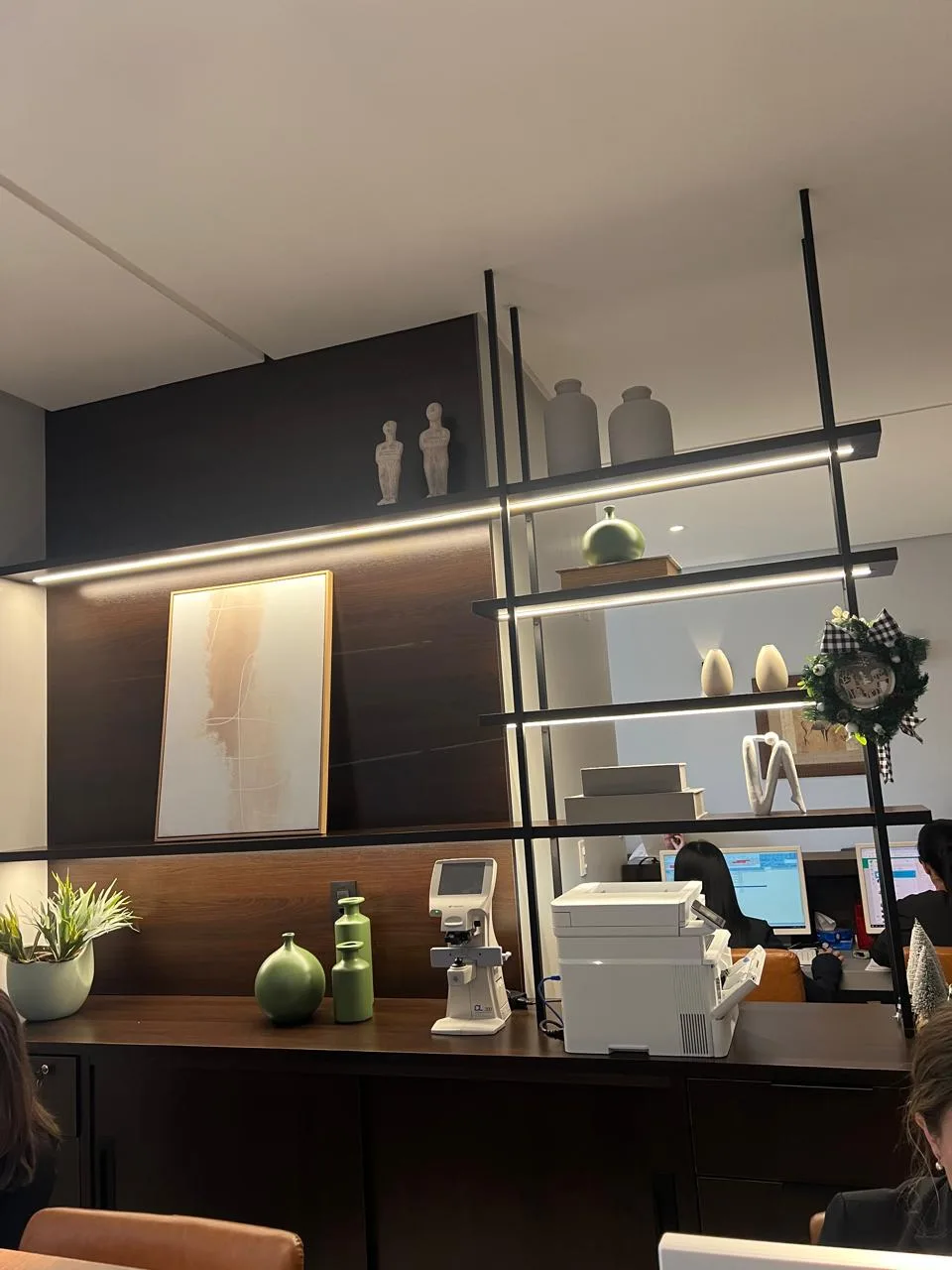 Recepção comercial com marcenaria escura, estante metálica e iluminação integrada