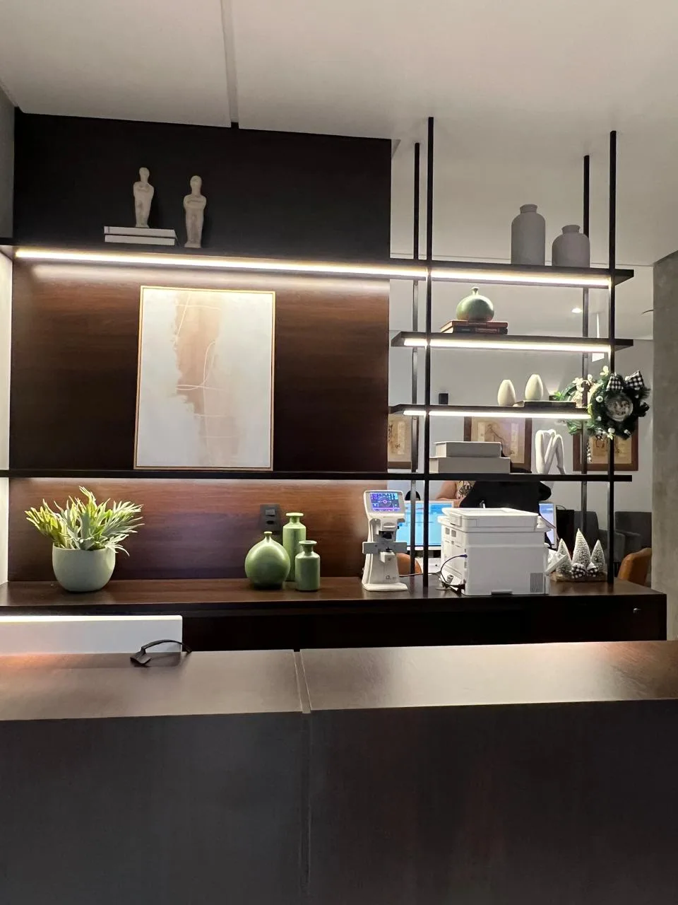 Balcão de recepção com marcenaria, objetos decorativos e iluminação linear