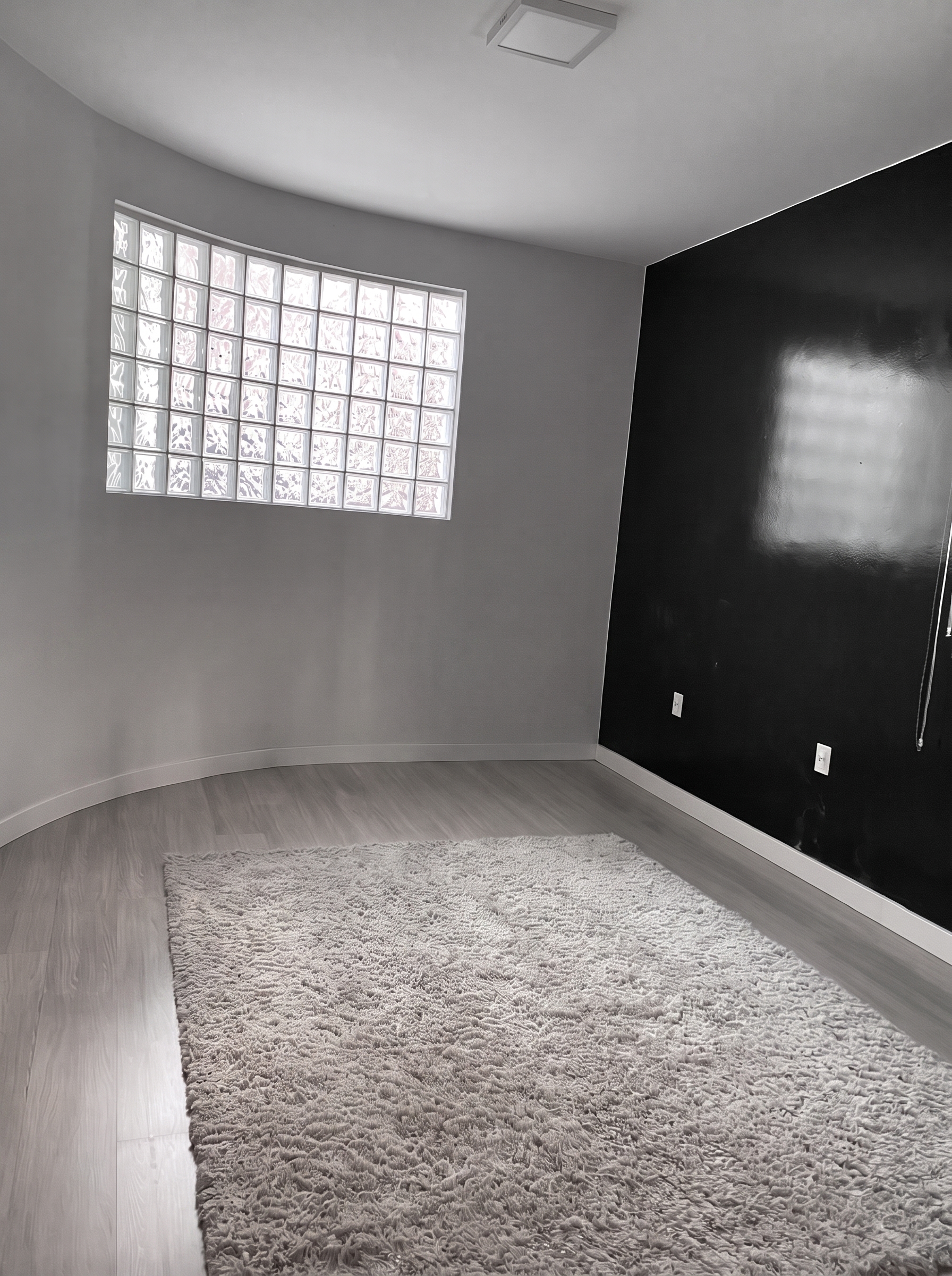 Ambiente durante a obra, com parede escura, janela de blocos de vidro e tapete claro