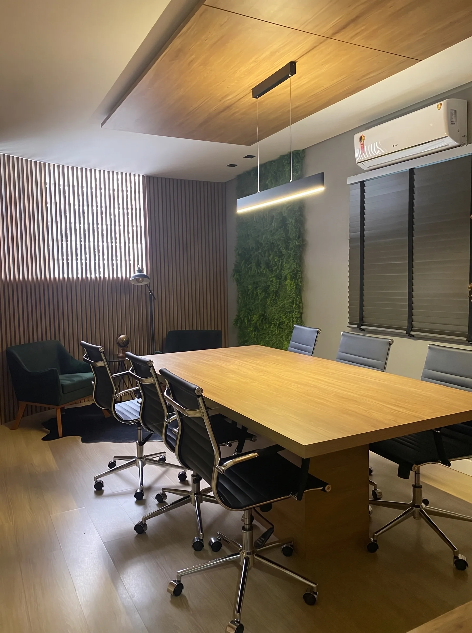Sala de reuniões concluída e mobiliada, com madeira, iluminação linear e jardim vertical